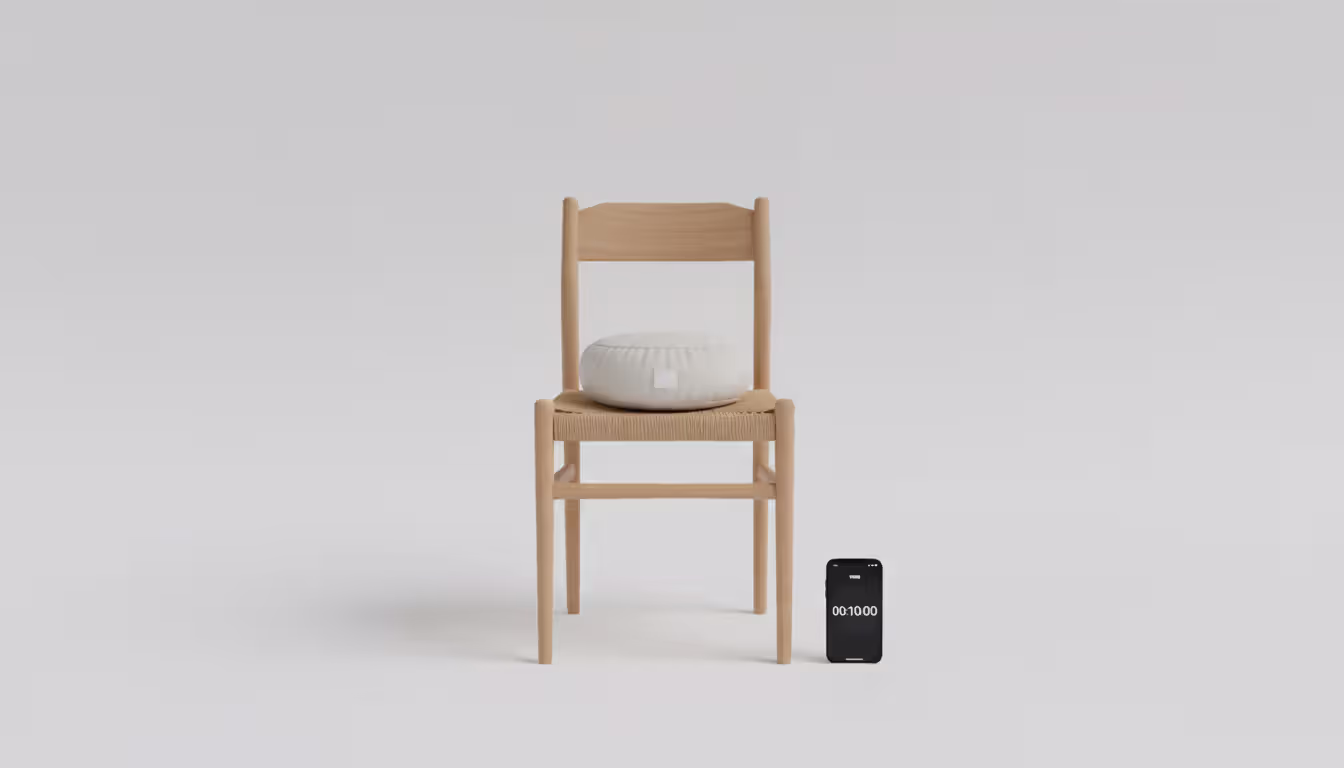 Simple meditation setup with a kitchen chair, small cushion, and smartphone showing a timer on a clean light background