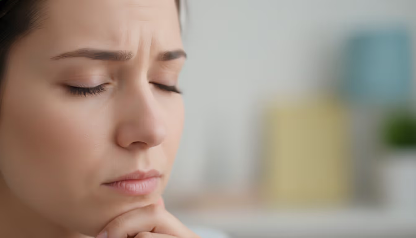 Close-up of a person with closed eyes and a slightly furrowed brow gently touching their chin in a moment of inner recognition and mindful self-reflection